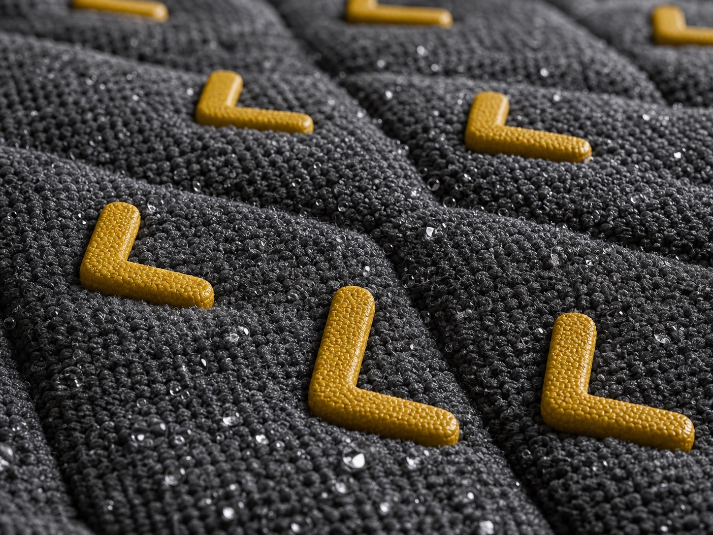 Macro view of the charcoal, water-beaded Signature L-Grip surface with raised yellow L details